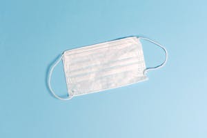 A disposable face mask lying on a light blue surface, symbolizing health protection.